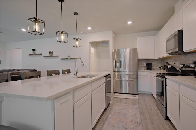 kitchen featuring a kitchen island with sink, decorative light fixtures, light wood-type flooring, stainless steel appliances, and sink