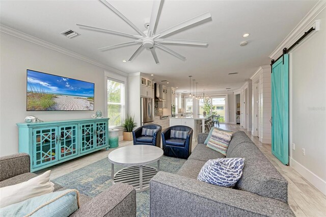 living room with ornamental molding, ceiling fan, a barn door, and a wealth of natural light