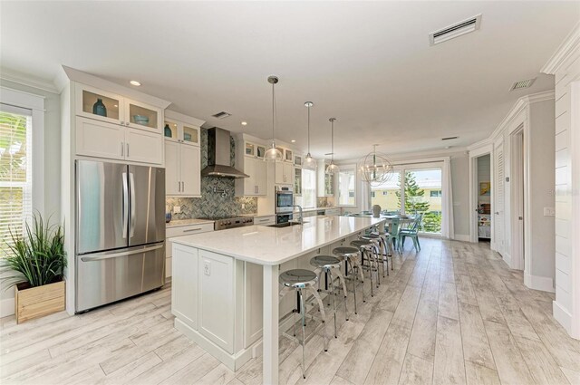 kitchen with appliances with stainless steel finishes, a breakfast bar area, a large island, tasteful backsplash, and wall chimney exhaust hood