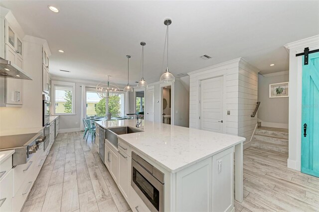 kitchen with a barn door, light hardwood / wood-style flooring, stainless steel appliances, a kitchen island with sink, and white cabinets