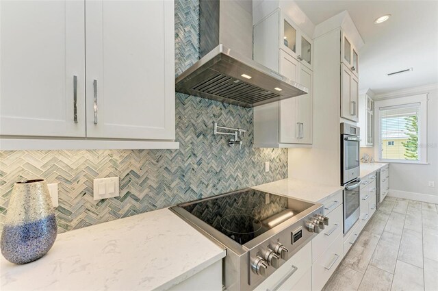 kitchen featuring light stone counters, tasteful backsplash, wall chimney exhaust hood, white cabinetry, and stovetop