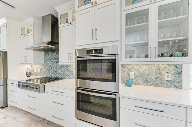 kitchen with wall chimney range hood, tasteful backsplash, white cabinetry, stainless steel appliances, and light stone countertops