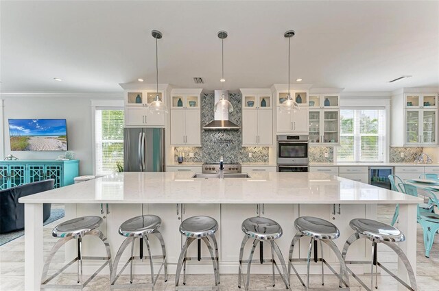 kitchen with a large island with sink, stainless steel appliances, a breakfast bar, and wall chimney exhaust hood