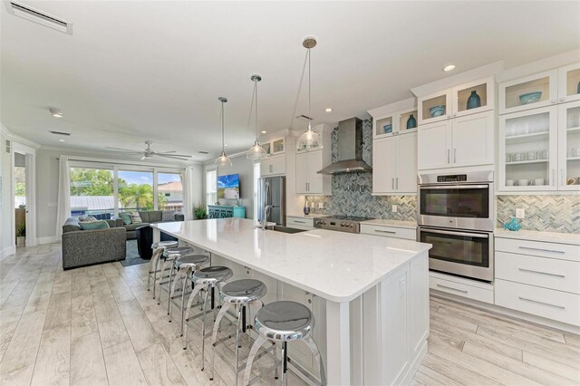 kitchen with stainless steel appliances, tasteful backsplash, wall chimney range hood, an island with sink, and a breakfast bar