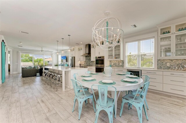 dining room with a healthy amount of sunlight, light wood-type flooring, and ceiling fan with notable chandelier