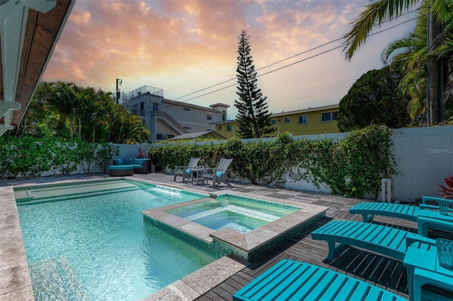 pool at dusk with a patio and an in ground hot tub