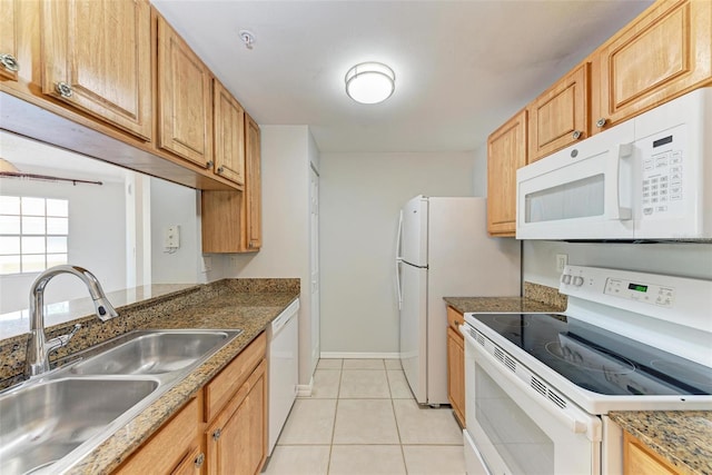 kitchen with sink, white appliances, light tile floors, and dark stone counters