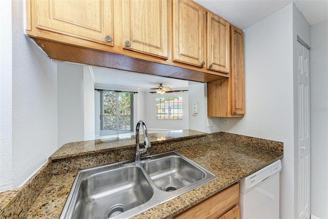 kitchen with white dishwasher, dark stone counters, ceiling fan, and sink