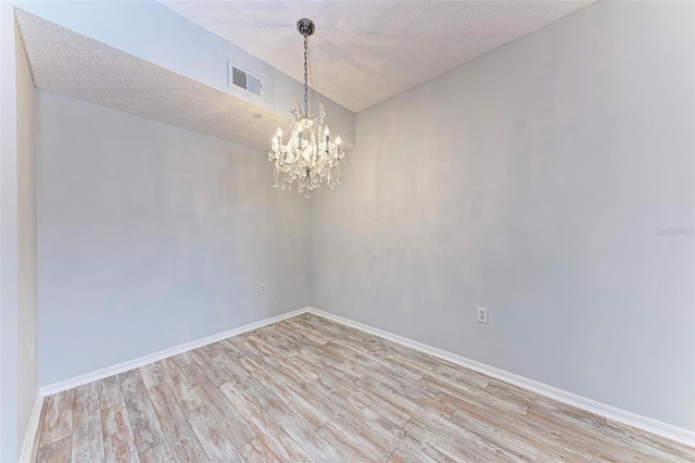 spare room featuring a textured ceiling, light hardwood / wood-style flooring, and an inviting chandelier