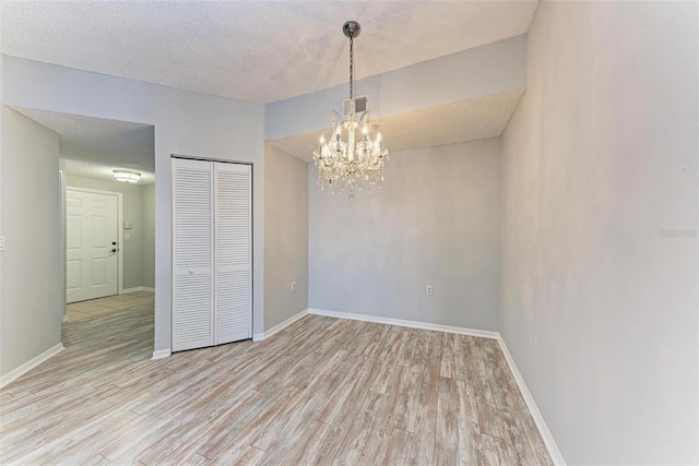 unfurnished bedroom with a closet, a textured ceiling, light wood-type flooring, and a chandelier