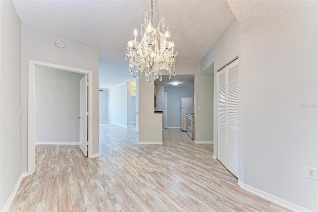 empty room featuring light hardwood / wood-style floors, a notable chandelier, and a textured ceiling