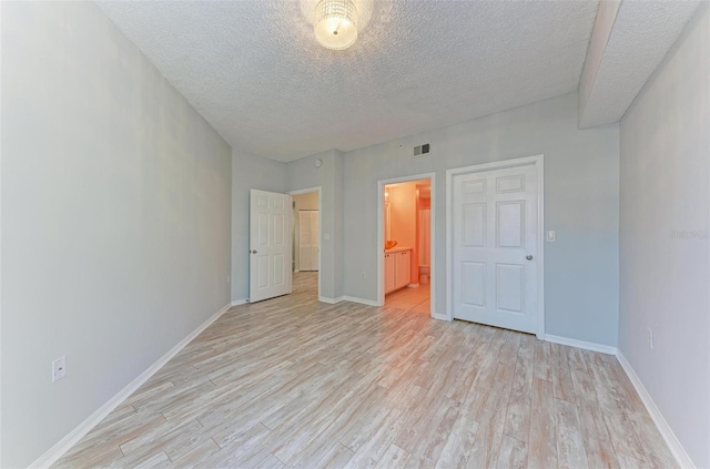 unfurnished bedroom with light wood-type flooring, ensuite bathroom, and a textured ceiling