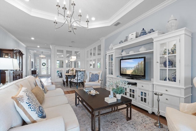 living room with a chandelier, hardwood / wood-style flooring, a raised ceiling, and ornamental molding