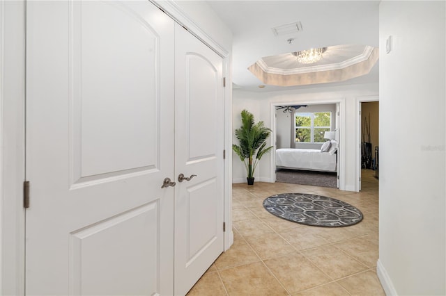 hallway with ornamental molding, a tray ceiling, and an inviting chandelier