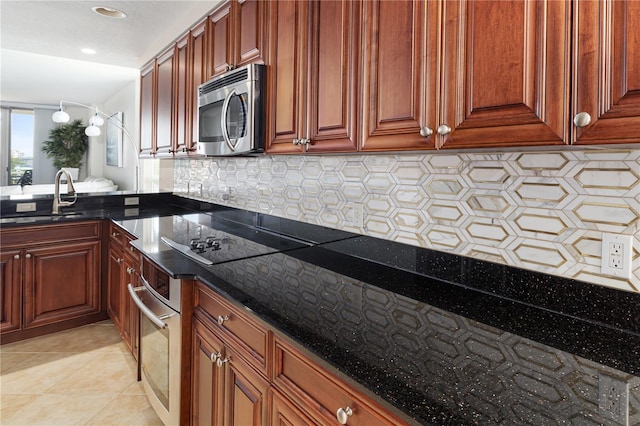 kitchen with backsplash, appliances with stainless steel finishes, light tile floors, sink, and dark stone countertops