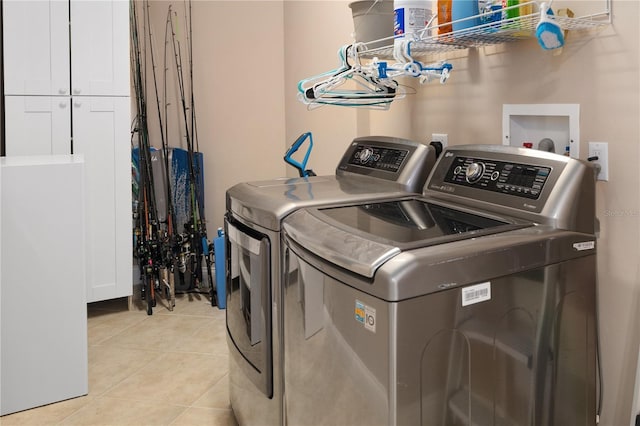 clothes washing area featuring cabinets, light tile floors, and washer and dryer