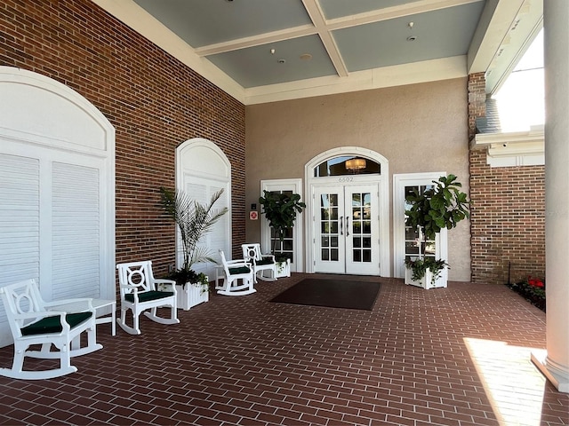 entrance to property featuring french doors, brick siding, covered porch, and stucco siding