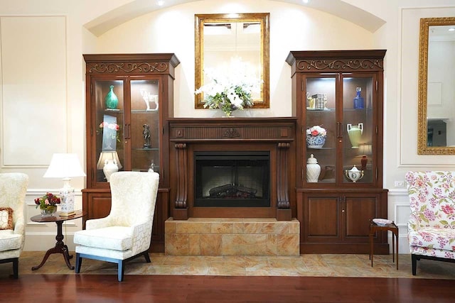 sitting room with crown molding, a glass covered fireplace, a decorative wall, and wood finished floors