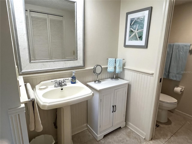 bathroom featuring a wainscoted wall, a closet, toilet, a sink, and tile patterned flooring