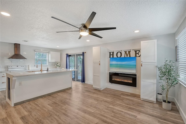 kitchen featuring wall chimney exhaust hood, light wood-type flooring, white cabinetry, and white stove