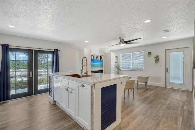 kitchen with an island with sink, white cabinets, a textured ceiling, and sink