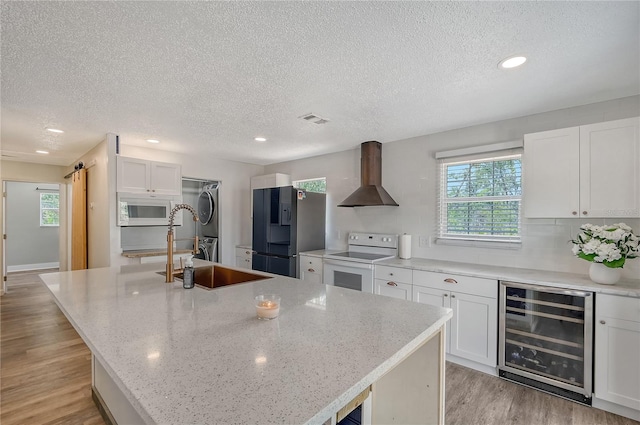 kitchen featuring wine cooler, a kitchen island with sink, white cabinets, a barn door, and white appliances