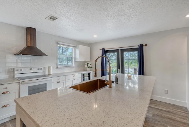 kitchen with white cabinets, white electric range, a center island with sink, and wall chimney range hood