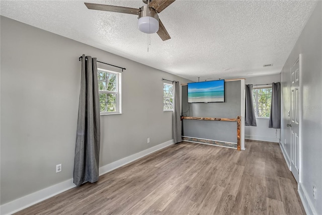 unfurnished living room with a wealth of natural light, light hardwood / wood-style floors, ceiling fan, and a textured ceiling