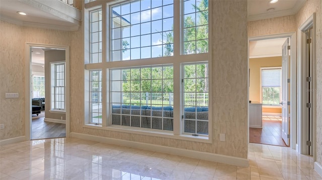 doorway featuring a healthy amount of sunlight, crown molding, and light tile floors