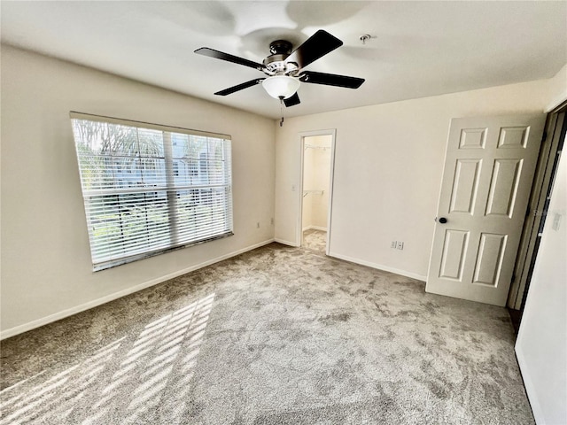 unfurnished bedroom featuring a closet, light colored carpet, a spacious closet, and ceiling fan