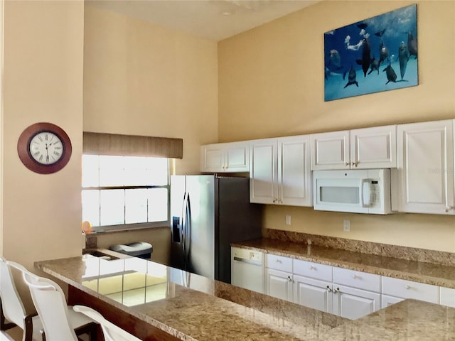 kitchen featuring a kitchen breakfast bar, white cabinetry, light stone countertops, and white appliances