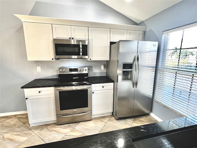 kitchen featuring stainless steel appliances, vaulted ceiling, light tile patterned floors, dark stone countertops, and white cabinets