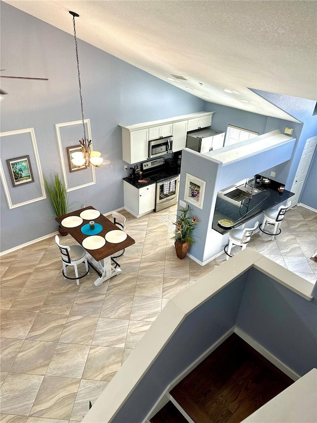 kitchen with stainless steel appliances, vaulted ceiling, decorative light fixtures, a chandelier, and white cabinetry