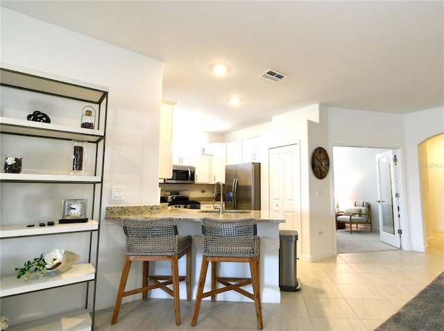 kitchen with light stone counters, kitchen peninsula, a kitchen breakfast bar, white cabinetry, and appliances with stainless steel finishes