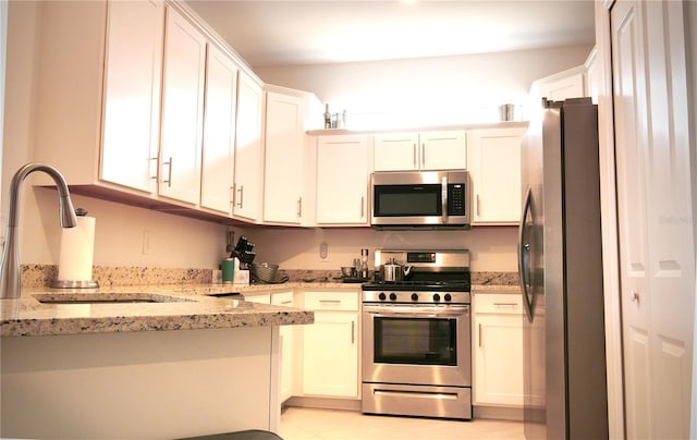 kitchen with light stone countertops, white cabinets, sink, light tile floors, and appliances with stainless steel finishes