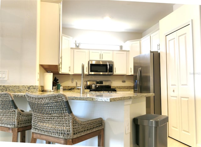 kitchen with white cabinets, a kitchen breakfast bar, appliances with stainless steel finishes, and kitchen peninsula