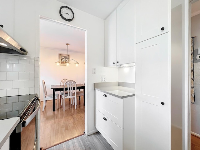 kitchen featuring hanging light fixtures, light hardwood / wood-style floors, backsplash, and white cabinetry