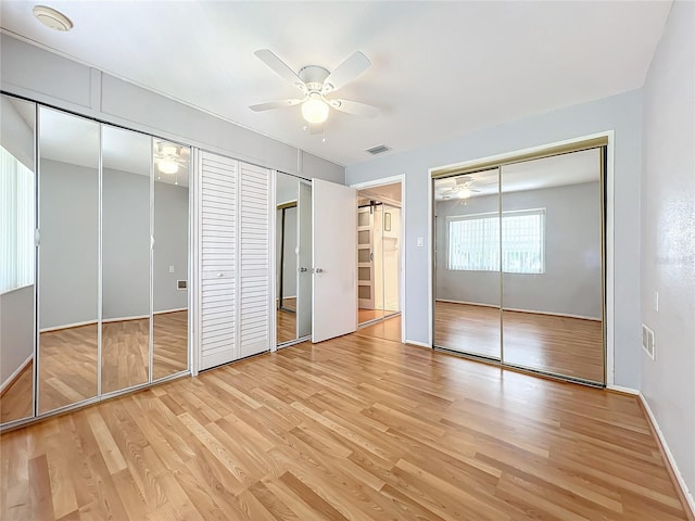 unfurnished bedroom with ceiling fan, two closets, and light wood-type flooring