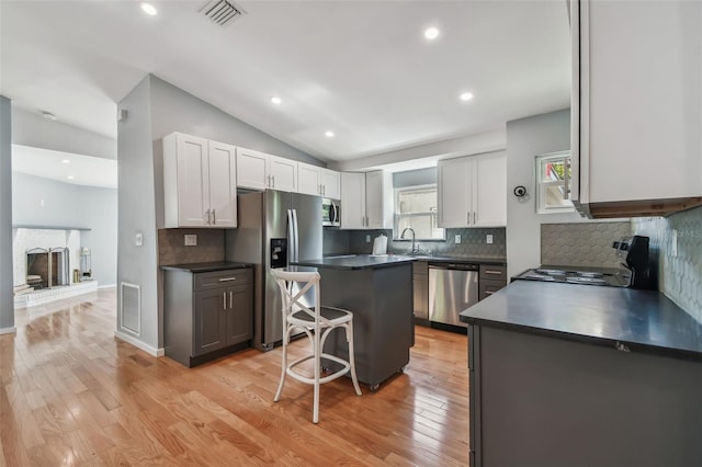 kitchen with a breakfast bar, lofted ceiling, a fireplace, a kitchen island, and stainless steel appliances