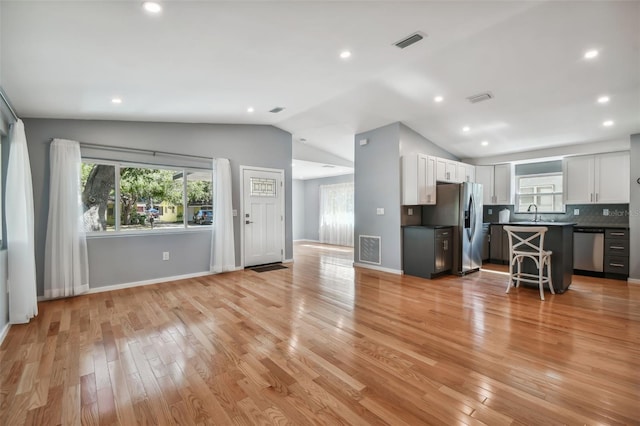 kitchen with lofted ceiling, decorative backsplash, appliances with stainless steel finishes, a kitchen island, and white cabinetry