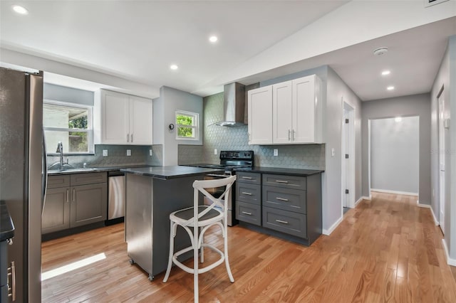 kitchen with stainless steel appliances, wall chimney range hood, a center island, gray cabinets, and white cabinetry