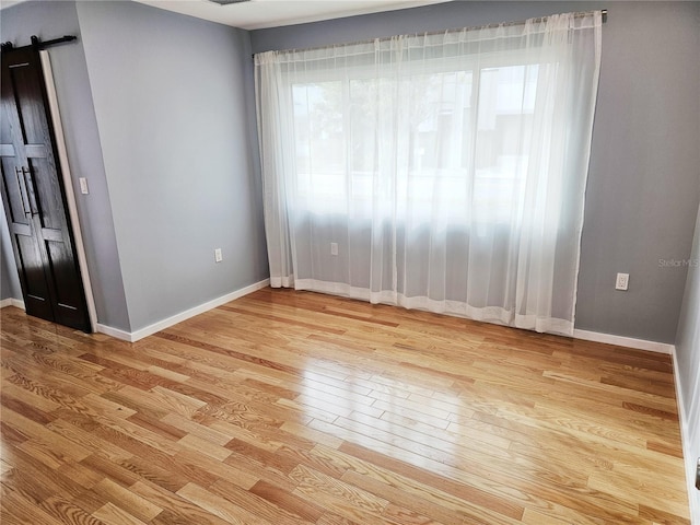 empty room featuring a barn door, a wealth of natural light, and light hardwood / wood-style flooring