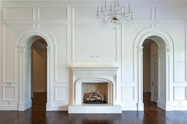 unfurnished living room with dark wood-type flooring, a notable chandelier, and decorative columns