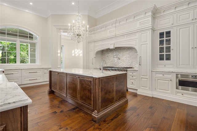 kitchen featuring dark hardwood / wood-style floors, backsplash, an inviting chandelier, stainless steel appliances, and an island with sink