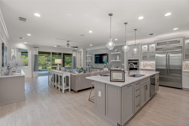 kitchen with ceiling fan, sink, stainless steel appliances, light hardwood / wood-style flooring, and a kitchen island with sink