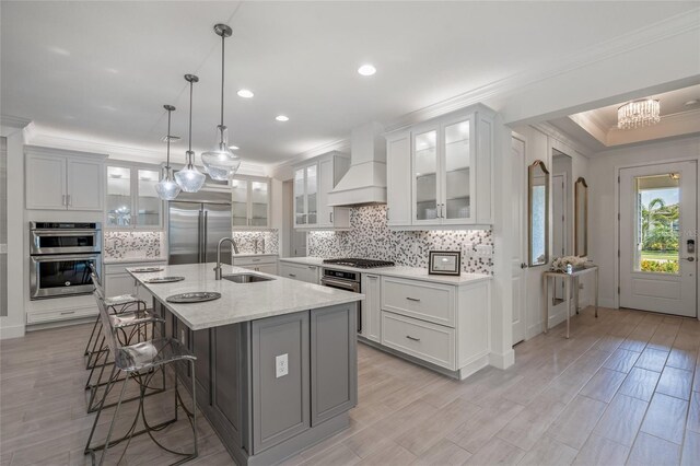 kitchen with premium range hood, backsplash, appliances with stainless steel finishes, an island with sink, and sink