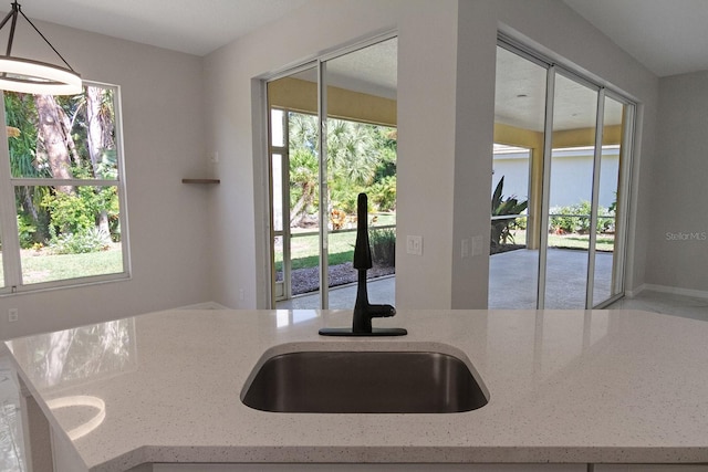 kitchen with light stone counters, sink, and decorative light fixtures