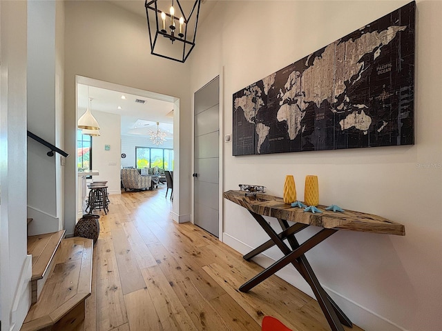 hallway with light hardwood / wood-style flooring, a towering ceiling, and a chandelier