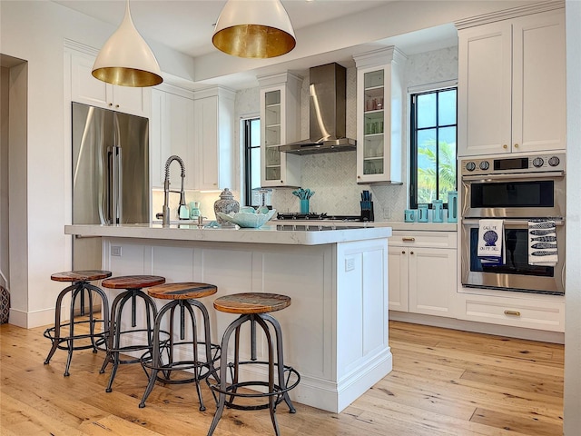 kitchen featuring white cabinets, backsplash, wall chimney range hood, stainless steel appliances, and light hardwood / wood-style floors