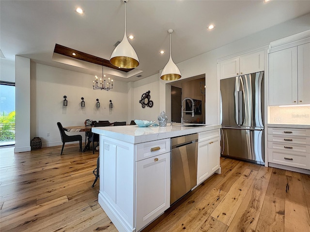 kitchen with appliances with stainless steel finishes, a center island with sink, white cabinets, sink, and light wood-type flooring